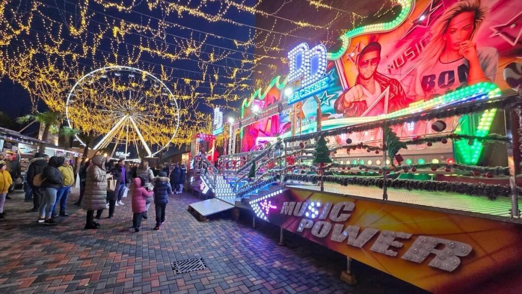 Vizitatori la Laminor Wonderland București, sub luminile festive, în fața atracției Music Power și a Roții Mari
