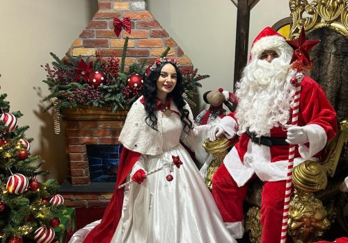 Moș Crăciun și Crăciunița în decor festiv cu brad și șemineu la Liftul lui Moș Crăciun, atracție de poveste pentru cei mici și părinți