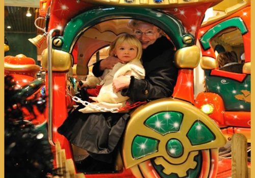 Copil și adult în Trenul Elfilor, atracție festivă de Crăciun cu decoruri colorate la Santa’s Land București