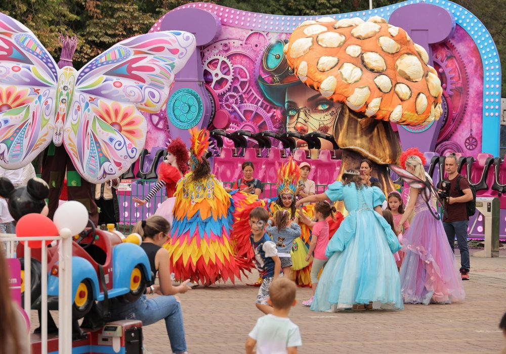 Personaje de poveste și artiști costumați în fluturi, ciuperci uriașe și păsări colorate, alături de copii la aniversarea de 10 ani Miramagica Park
